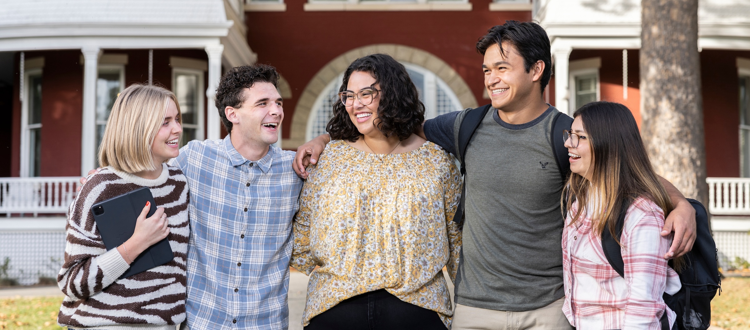 Five students laughing and smiling in front of Main Hall.