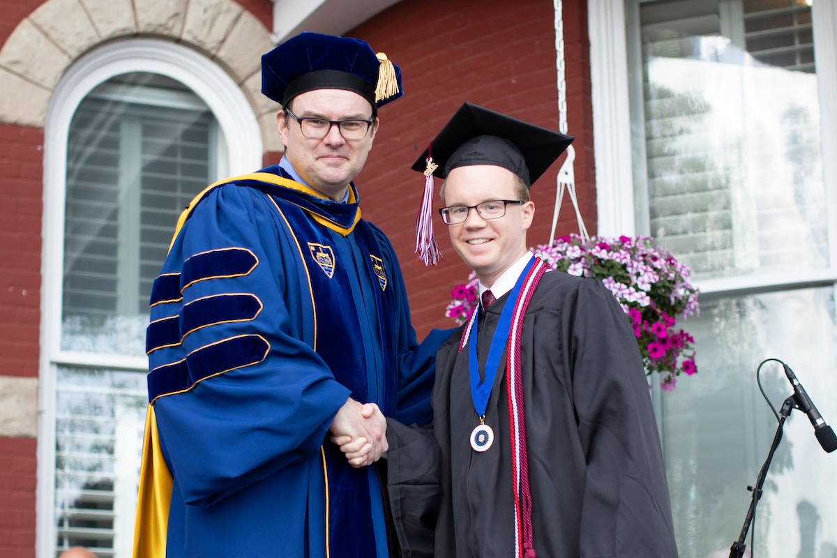Graduate Matthew Zalar shaking hands with a professor